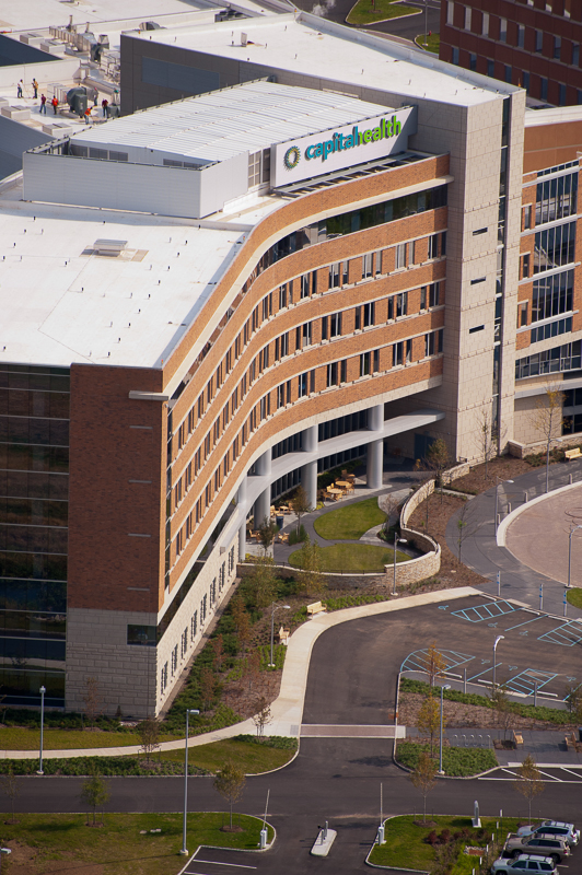Aerial view of a modern brick and glass hospital building with curved architecture and surrounding parking.